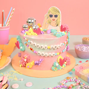 Decorative cake with a Taylor Swift motif, surrounded by party supplies against a pink background.