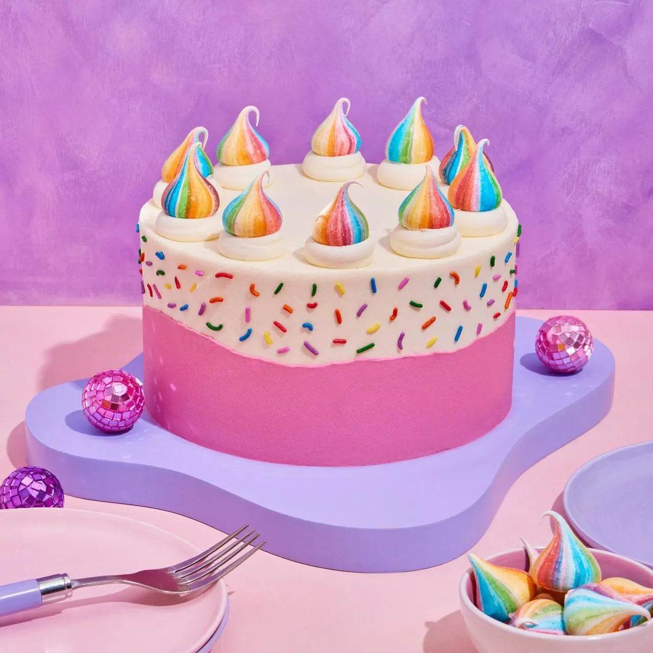 Birthday Cake by Crumbs & Doilies with pink buttercream, rainbow sprinkles, and unicorn poop meringue decorations.