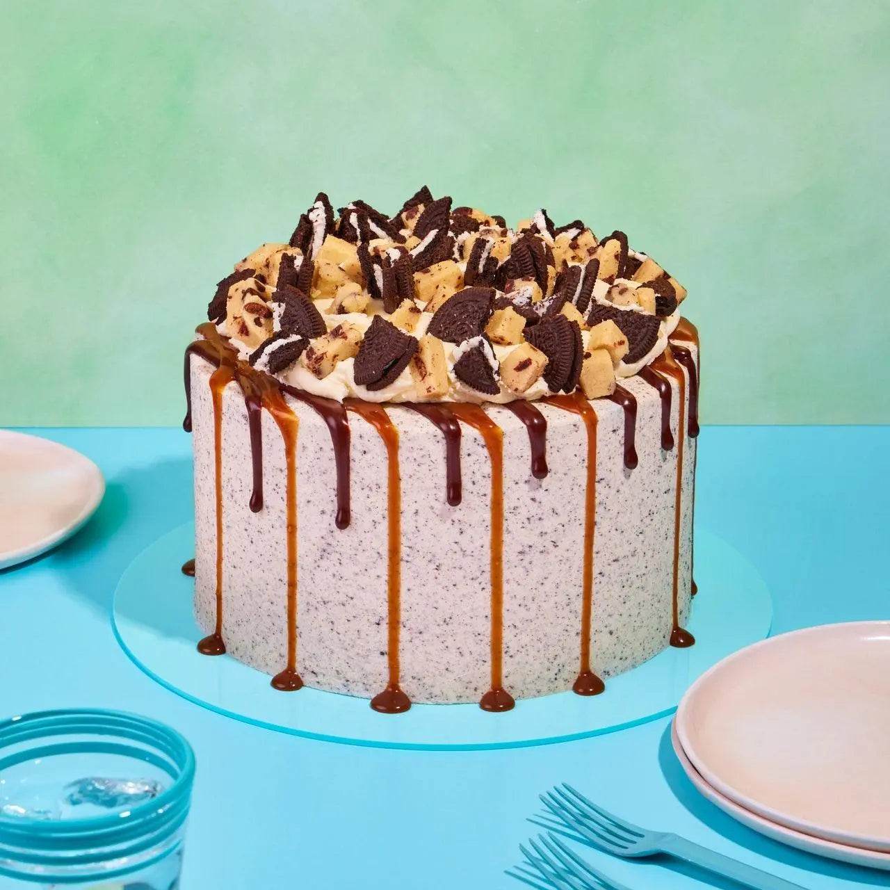 Red Velvet Volcano Cake by Crumbs & Doilies with Oreo crumb icing, cookie dough chunks, and caramel chocolate drip.