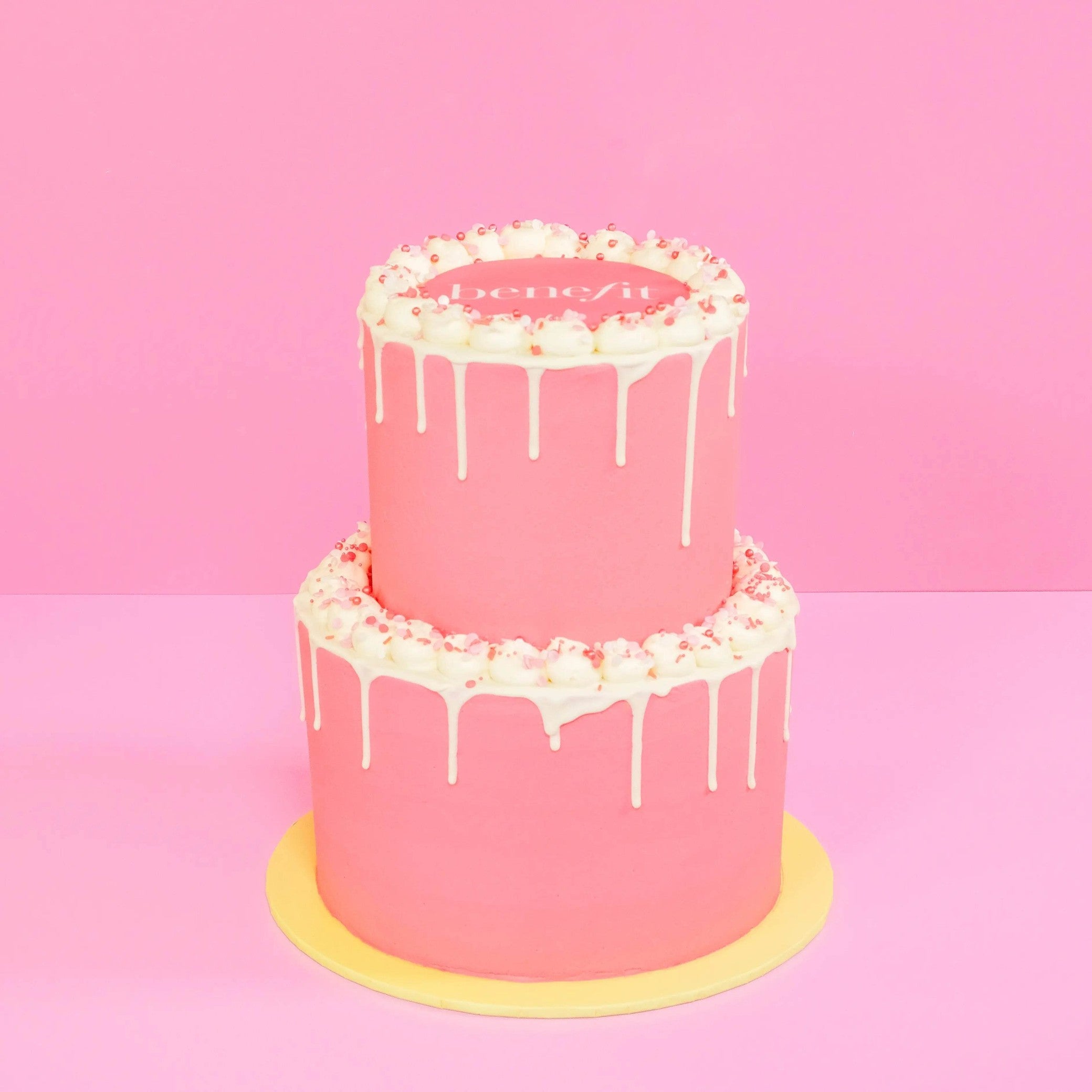 2 Tier Corporate Drip Cake with logo featuring pink Swiss Meringue icing and white drip decoration Crumbs & Doilies