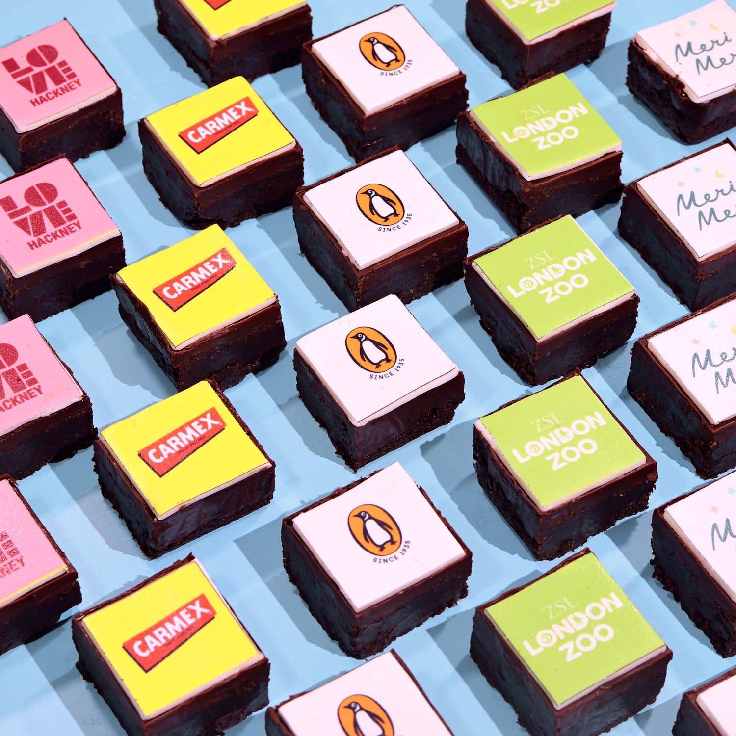 Gluten Free Almond Flour Corporate Brownies topped with colorful edible branded logo plaques arranged on blue background