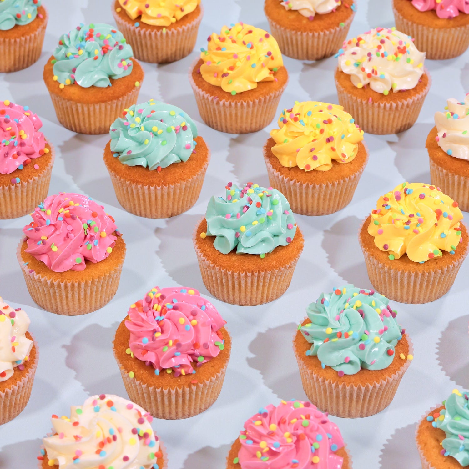 Gluten Free Vanilla Cupcakes with colorful swirled frosting and sprinkles arranged on a white surface.