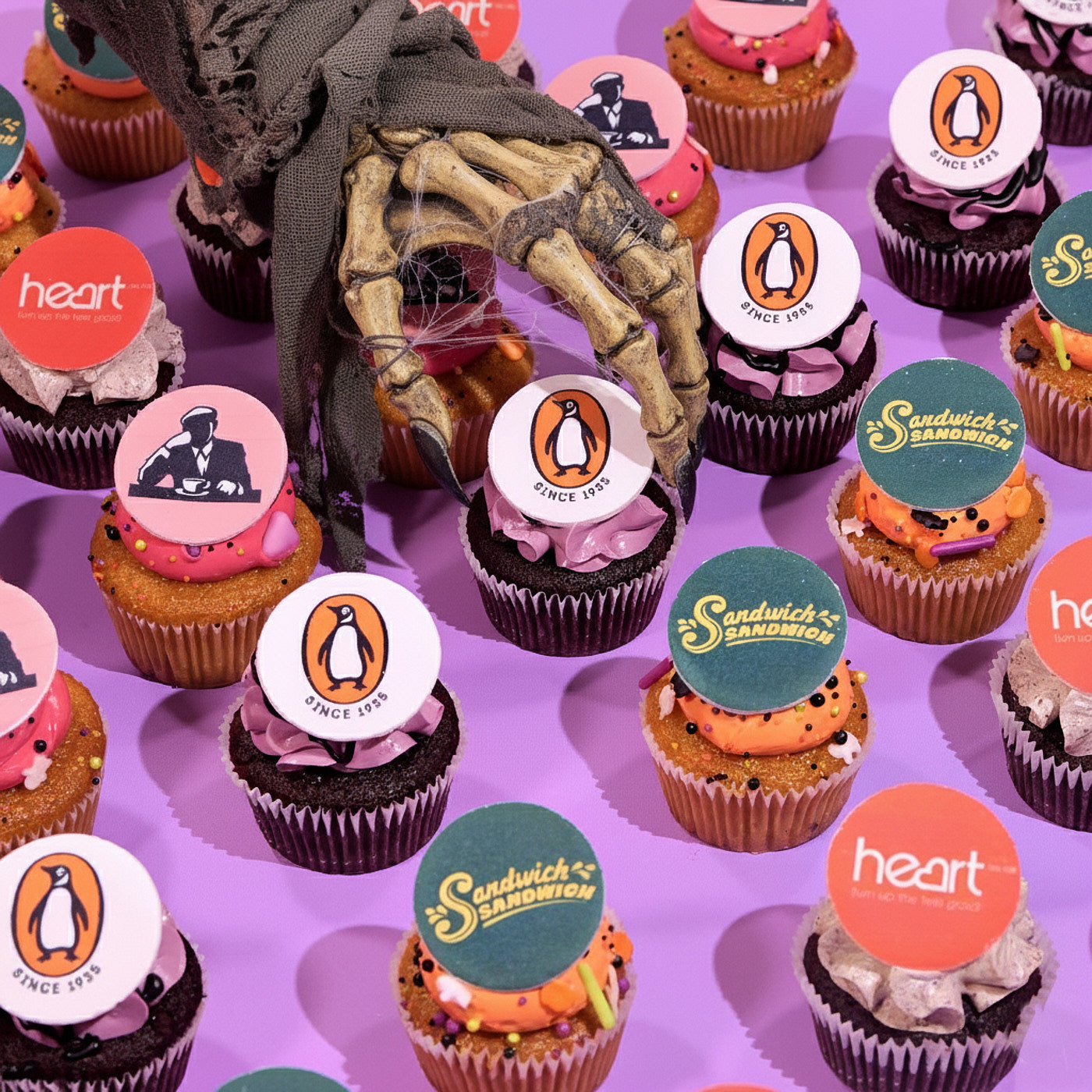 Halloween cupcakes with corporate logos and a spooky skeletal hand on a purple background for events and gifting