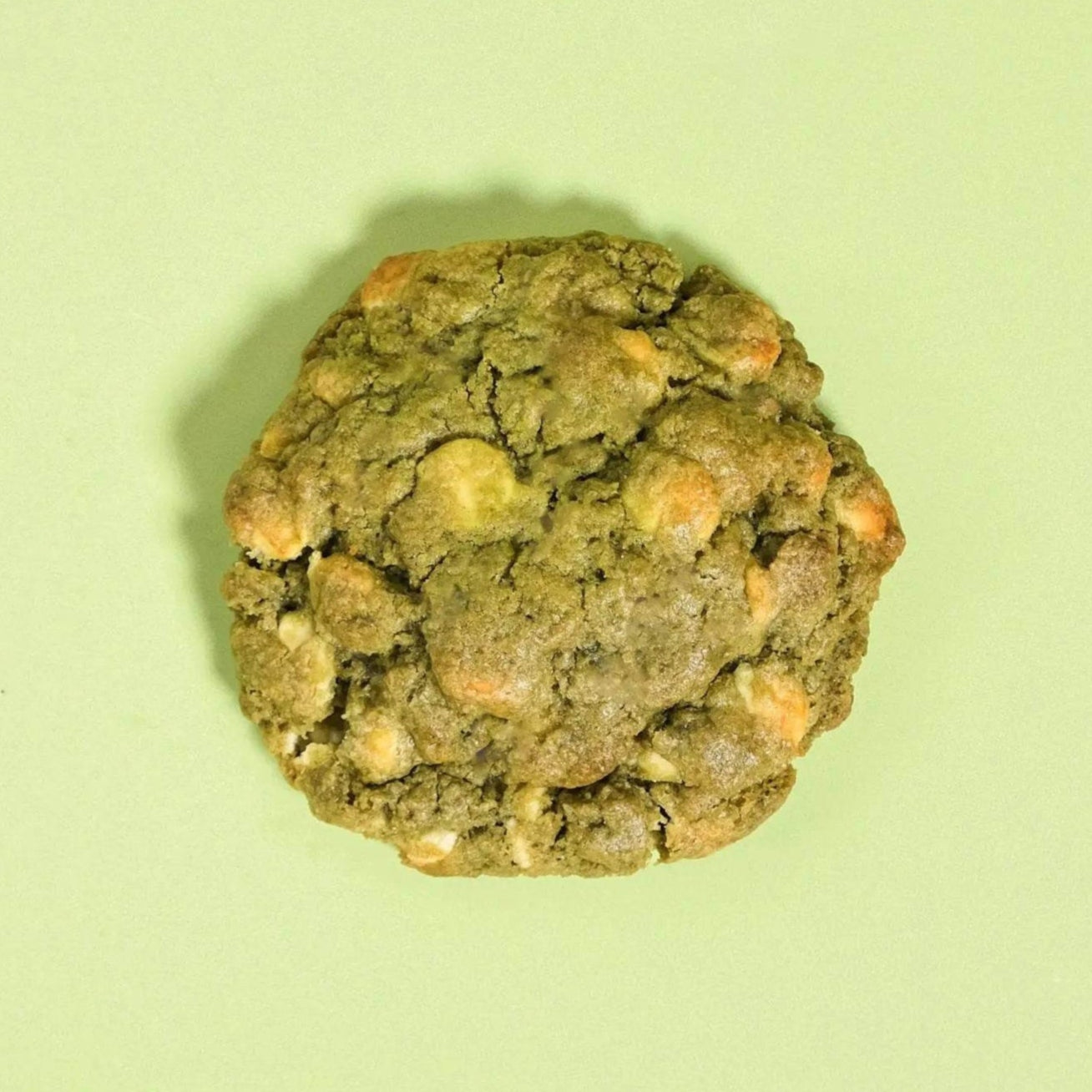 Matcha White Chocolate New York Cookie by Crumbs & Doilies, a green cookie with white chocolate chips on a light background.