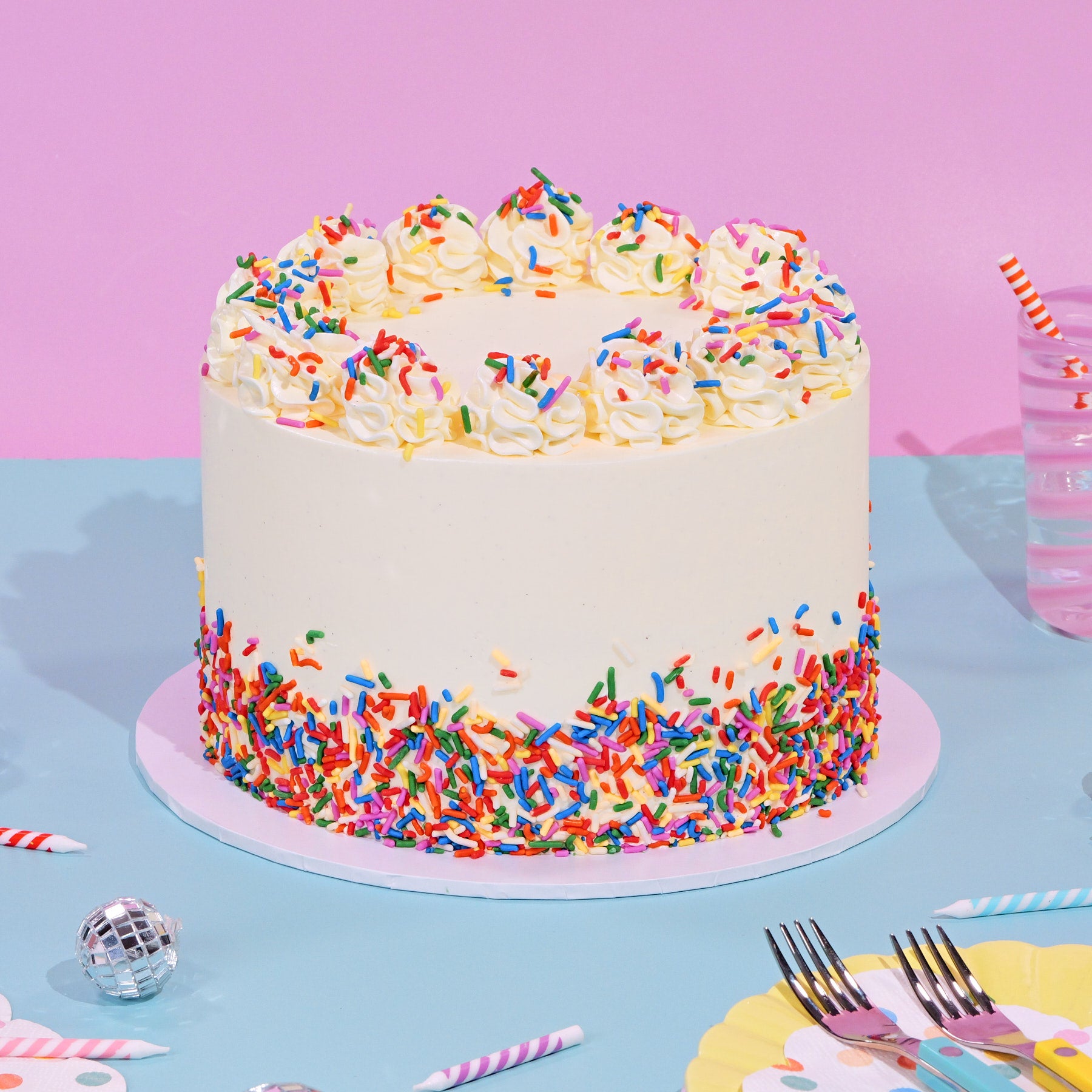 Red Velvet Birthday Cake with white frosting, colorful sprinkles decorating the base and piped cream swirls on top.