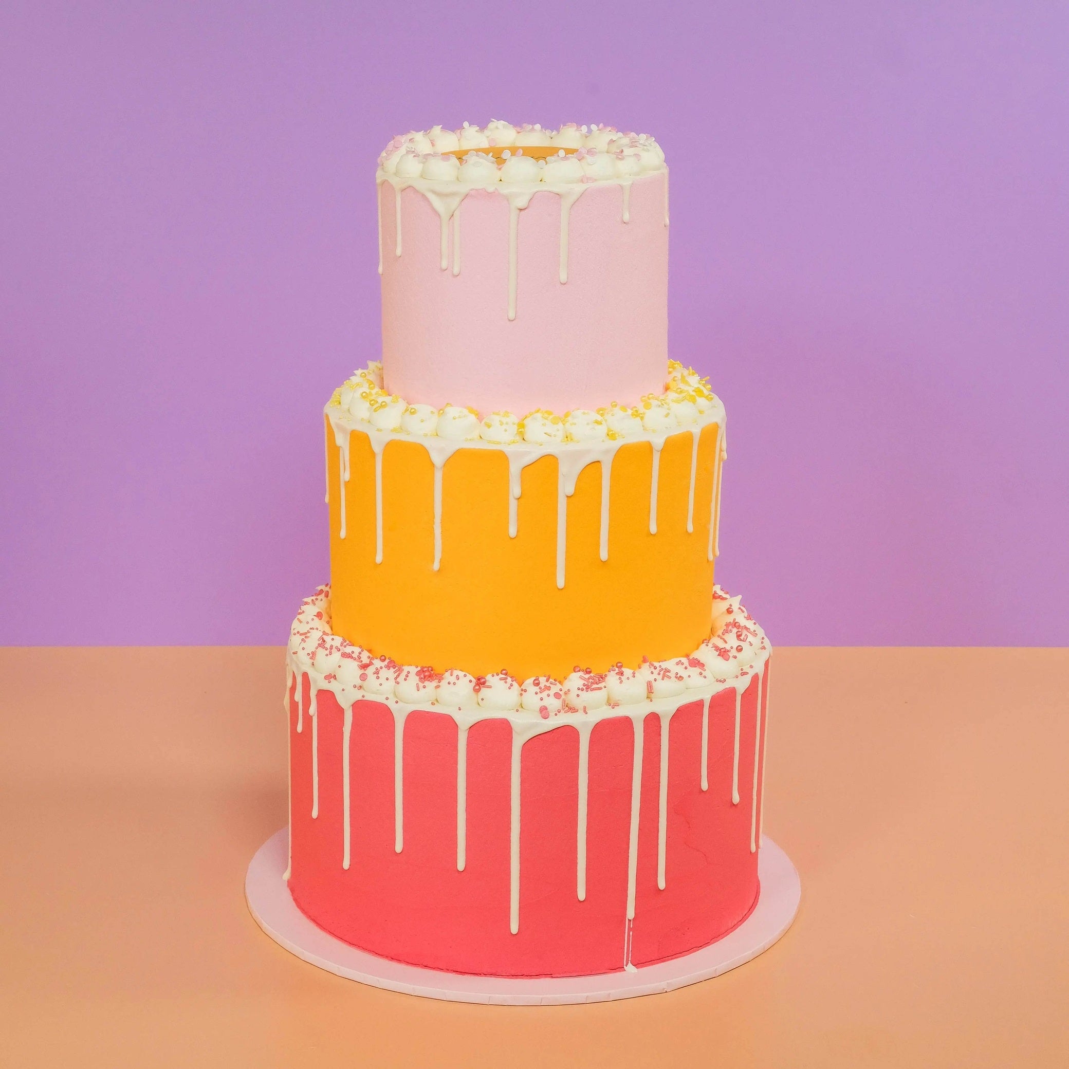 3 Tier Corporate Drip Cake with logo in pink, orange, and red layers by Crumbs & Doilies