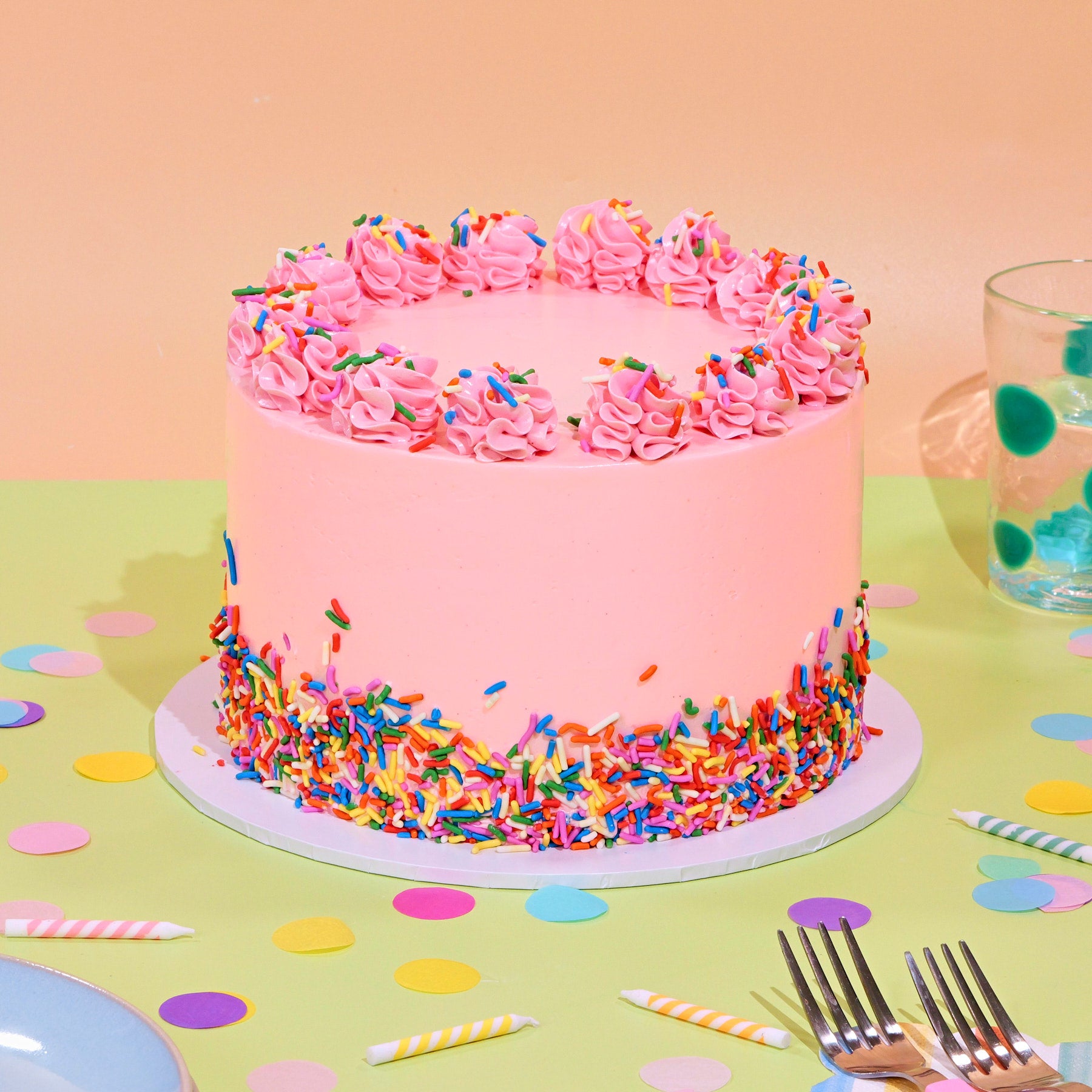 Vanilla Birthday Cake with pink frosting, swirled border, and colorful rainbow sprinkles decorating the base