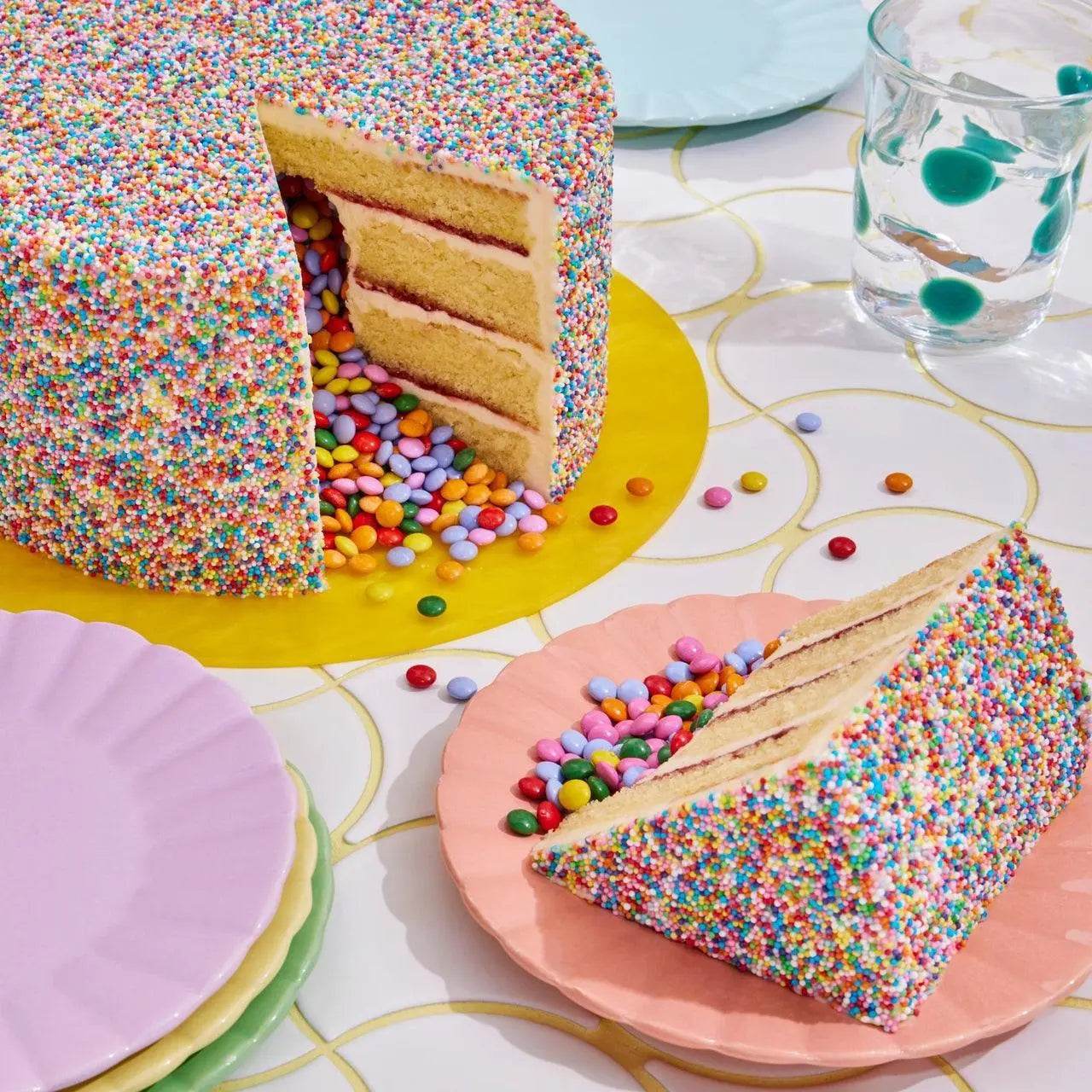 Pinata Cake with colorful rainbow sprinkles and mini Smarties spilling out from vanilla sponge layers.
