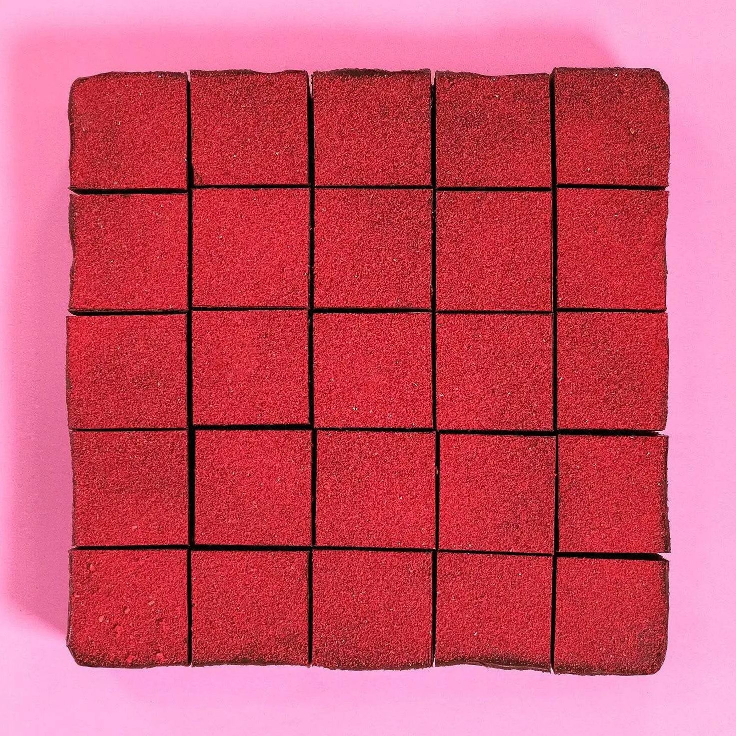 Raspberry & Dark Chocolate Brownie cut into squares with vibrant red topping on a pink background Crumbs & Doilies